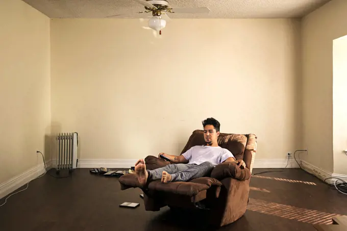 Man sitting in armchair watching television in barren apartment
