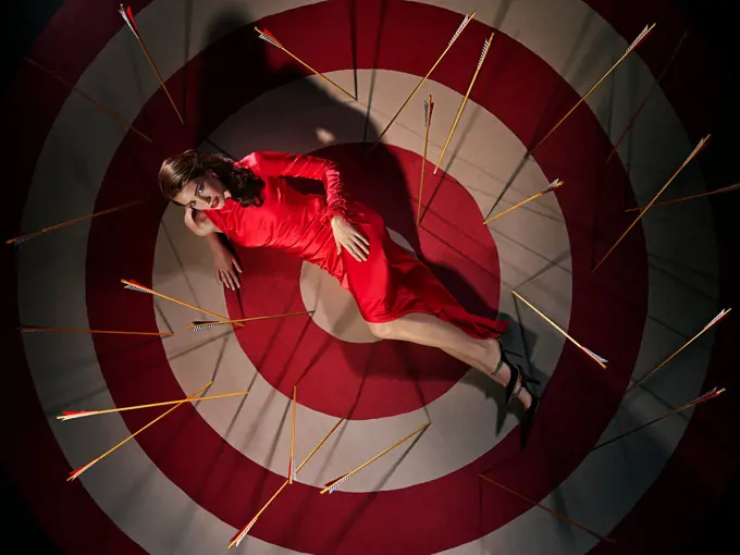 Overhead portrait of a woman laying on large hand painted Bulls-eye target with arrows
