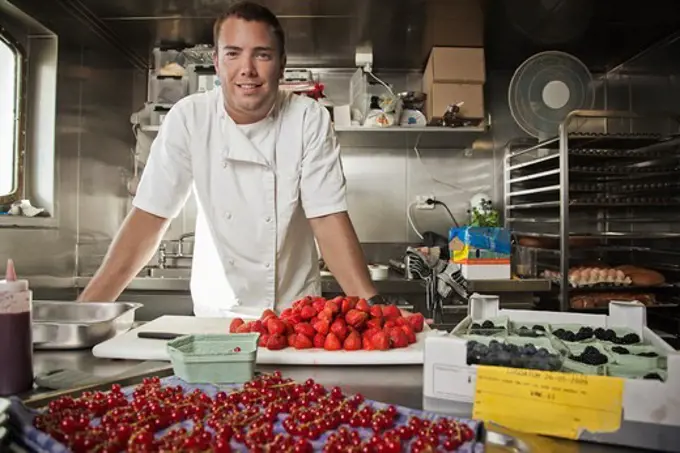 Pastry chef leaning on kitchen counter with assorted berries being prepped on counter