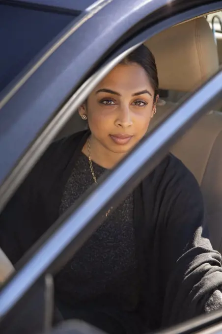 Portrait of woman sitting in drivers seat of car with door open, looking at camera 