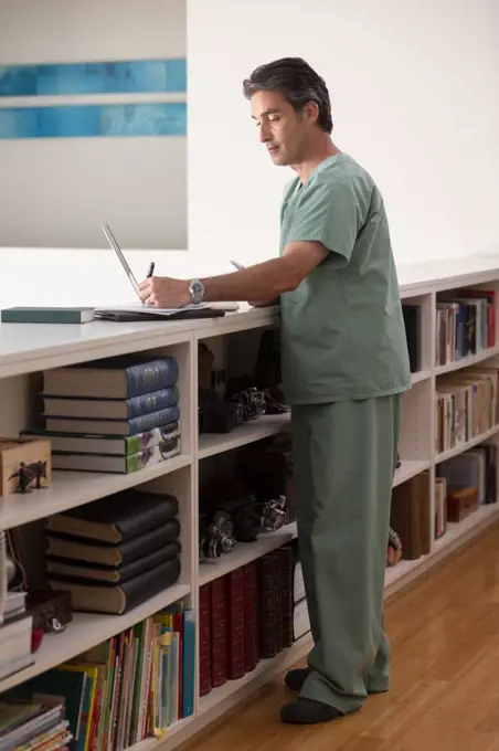 Hispanic Male doctor in his home practicing Telemedicine taking notes 