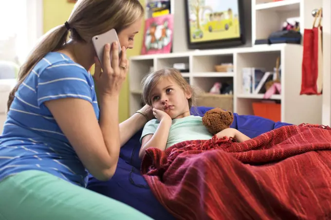 Mom with daughter who is not feeling well using cell phone to consult doctor and get advice via Telemedicine service 