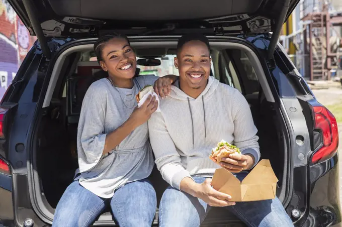 Portrait of young African American couple having impromptu picnic lunch in the back of their vehicle.