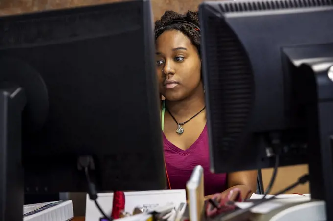 A portrait of an African American woman at her call center desk and her headset on focusing on her computer monitor.