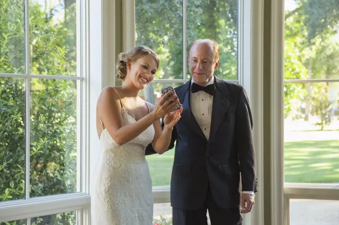 Bride showing her father picture on mobile phone screen 