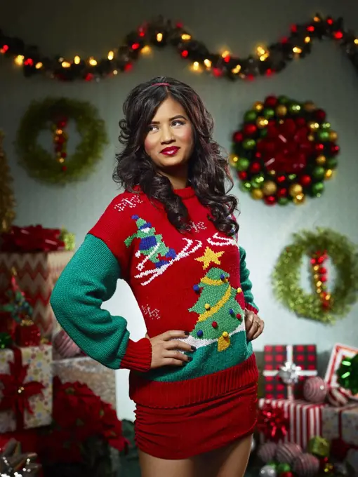Portrait of woman in ugly Christmas sweater looking off camera against a Christmas themed backdrop.
