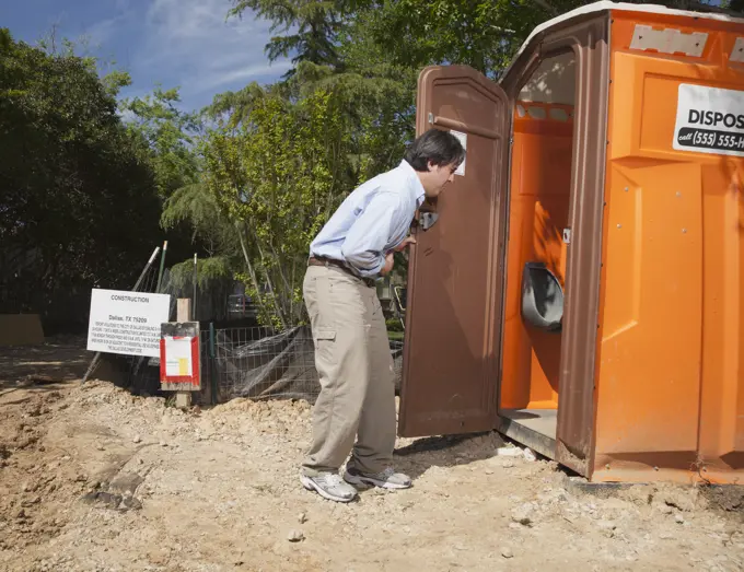 Man holding his stomach while entering a portable toilet at a residential construction site