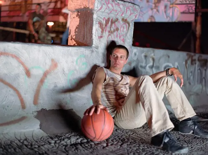 Man leaning against a wall and holding a basketball