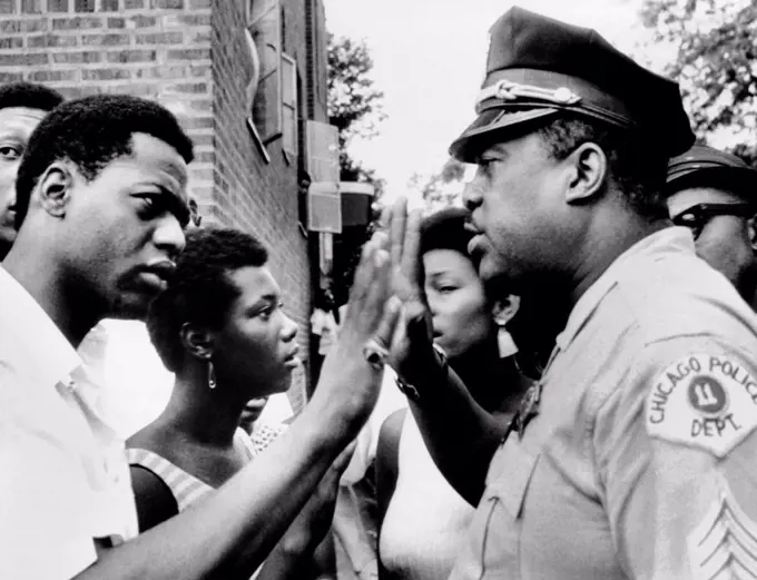 Chicago African American policeman tries to calm a crowd. Violence broke out for the second night in a row on the southwest side. July 13, 1966.
