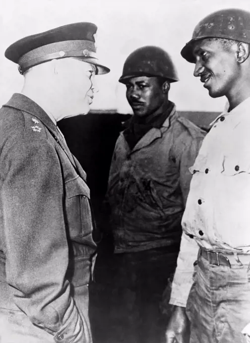 General Dwight Eisenhower talking with two African American soldiers at the supply port of Cherbourg, France. Eisenhower commanded a segregated US military during World War II.
