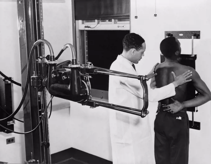 African American doctor placing patient in the correct position for taking chest x-ray for use in the diagnosis in 1937.