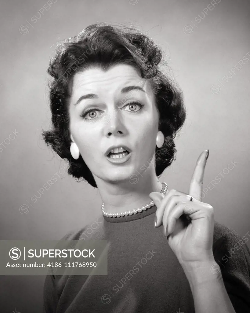 1950s 1960s BRUNETTE WOMAN PEARL STRAND EARRINGS POINTING FINGER UP SPEAKING TALKING LOOKING AT CAMERA LECTURE TEACH NAG