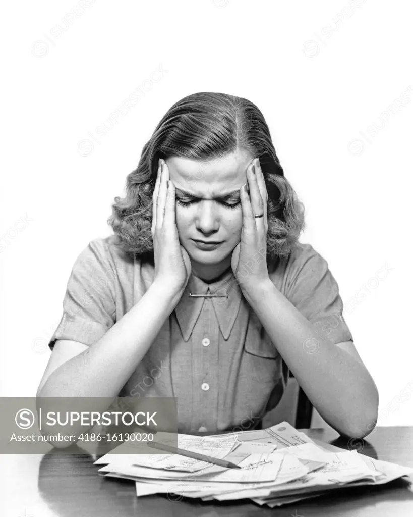 1940s PANIC STRICKEN OVERWHELMED WOMAN HOLDING HER HEAD LOOKING DOWN AT PILE OF UNPAID BILLS ON THE TABLE 