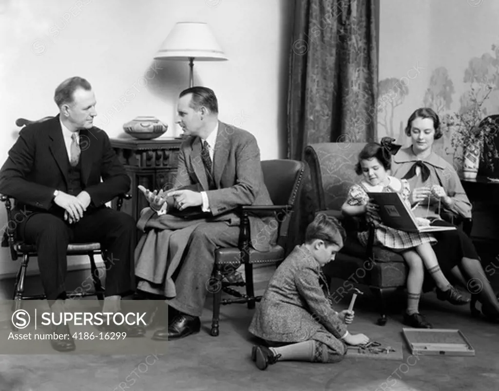 1930S Family In Living Room Mother Knits Daughter On Her Lap With Book Son On Floor With Hammer