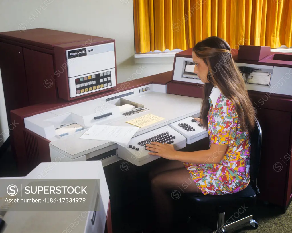 1960s YOUNG WOMAN OPERATING A HONEYWELL BUSINESS COMPUTER ENTERING DATA ON KEYBOARD