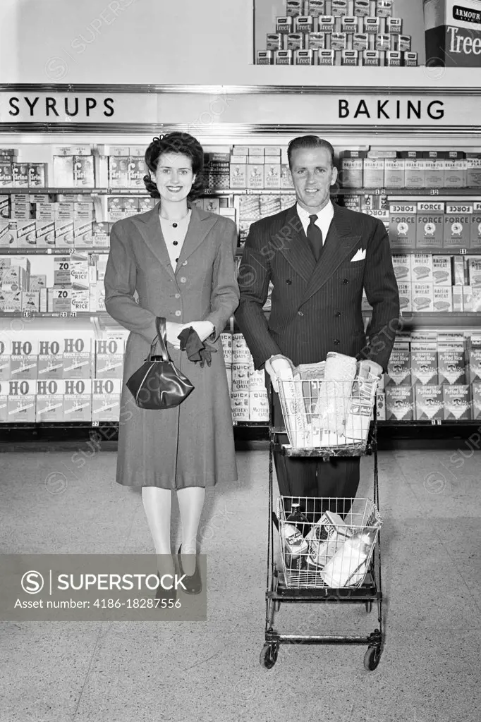 1940s MAN AND WOMAN COUPLE SHOPPING IN GROCERY STORE MAN PUSHING GROCERY CART