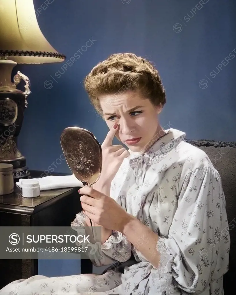 1950s 1960s WOMAN IN NIGHTGOWN HOLDING MIRROR LOOK AT EYE WRINKLES AGING BEAUTY COSMETIC SERIOUS CONCERNED EXPRESSION