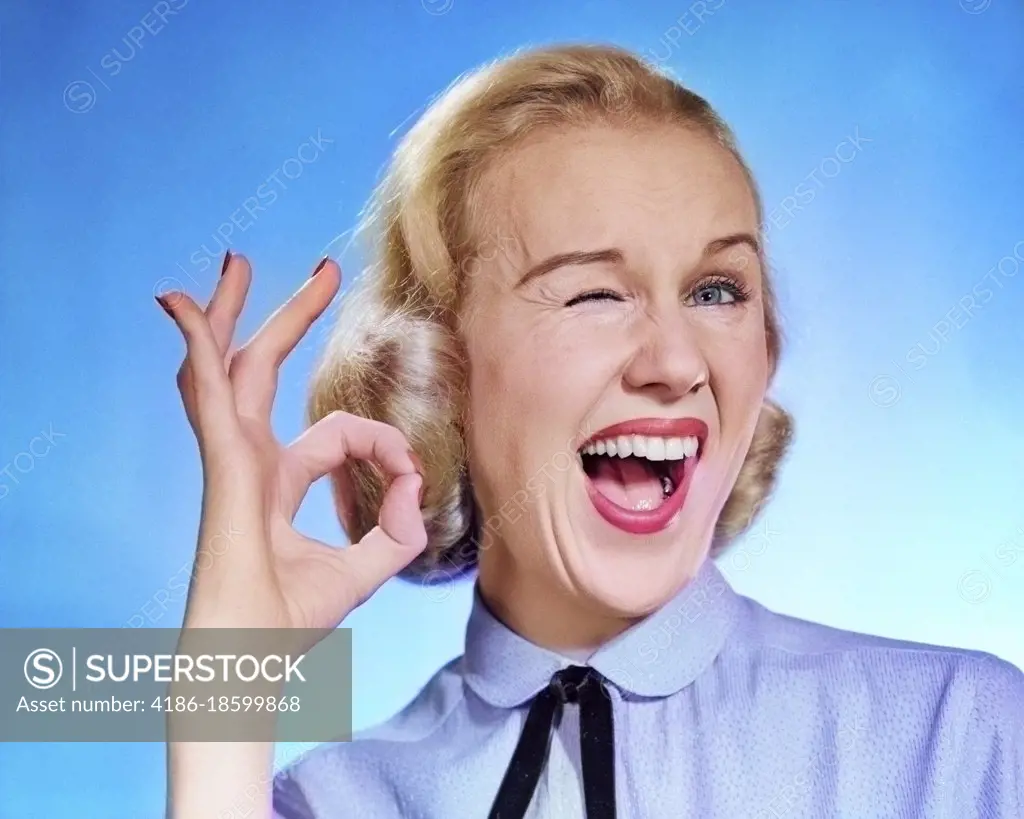 1950s ENTHUSIASTIC BLOND WOMAN MOUTH OPEN WINKING EYE LOOKING AT CAMERA AND MAKING OK SIGN WITH THUMB AND FINGER