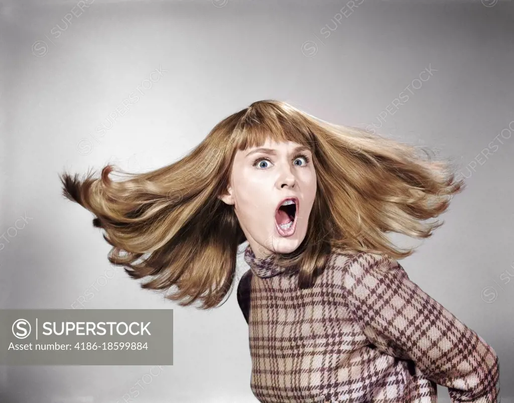 1960s PORTRAIT OF SURPRISED RED HAIR WOMAN LOOKING AT CAMERA WITH MOUTH WIDE OPEN AND HAIR FLYING
