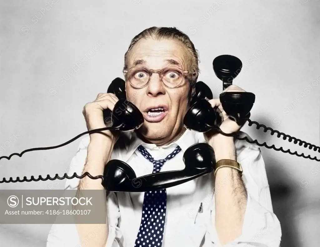 1950s 1960s PORTRAIT OF FRAZZLED BUSINESSMAN TRYING TO ANSWER FOUR BLACK TELEPHONES PHONES AT ONCE