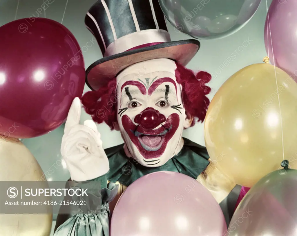 1950s CIRCUS CLOWN PORTRAIT SMILING AMID BALLOONS POINTING UP LOOKING AT CAMERA