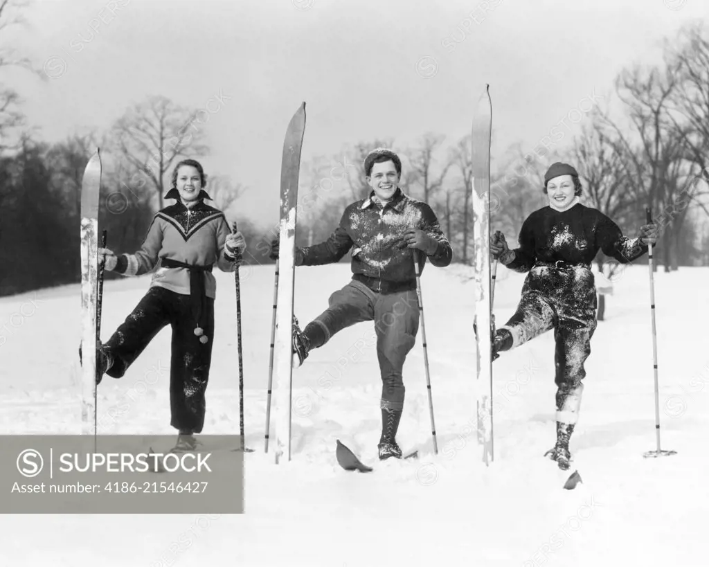 1930s TWO WOMEN AND A MAN LOOKING AT CAMERA SMILING POSING ON SKIS WITH RIGHT SKI TURNED UPRIGHT 