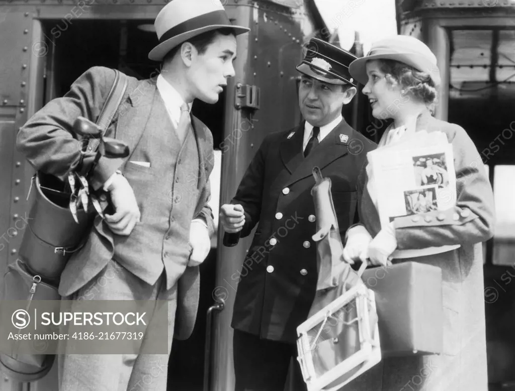 1930s COUPLE STANDING BY TRAIN WORRIED MAN WITH GOLF CLUBS WOMAN WITH TENNIS RACQUET CONDUCTOR ASKING FOR MISPLACED TICKET