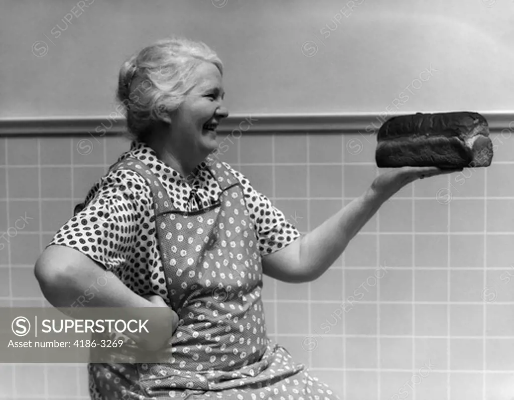 1930S 1940S Grandmother In Apron Admiring Loaf Of Freshly Baked Bread