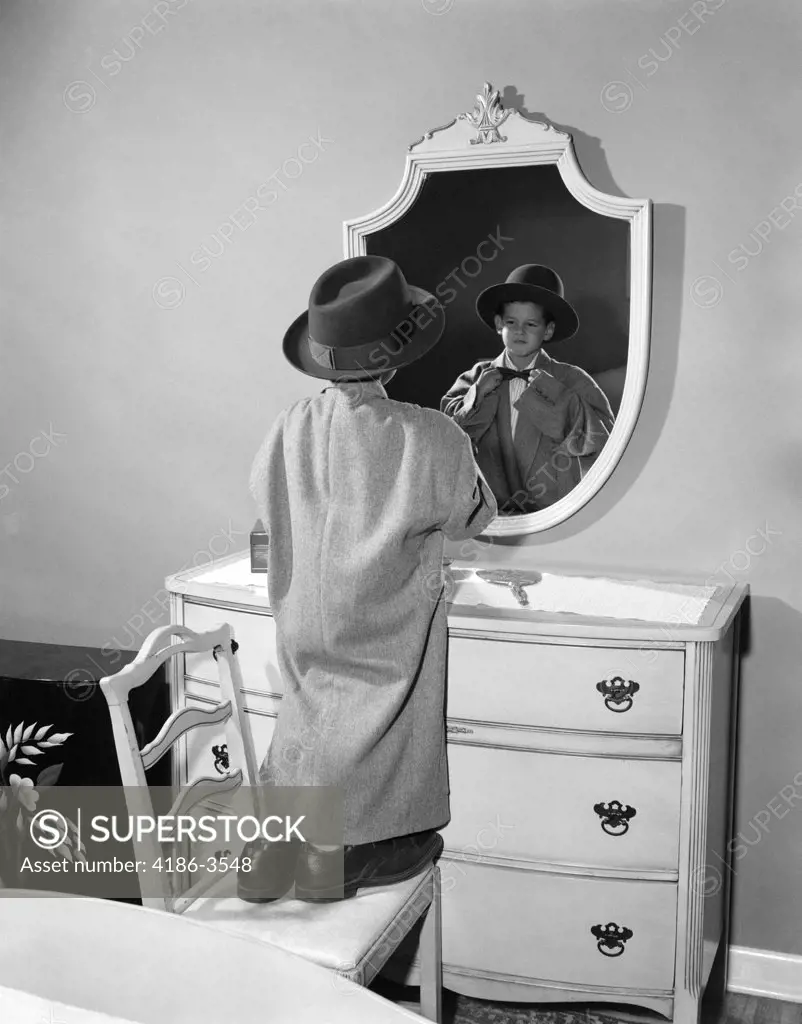 1950S Boy Dressed In Father'S Hat Coat & Shoes Standing On Chair Looking In Mirror