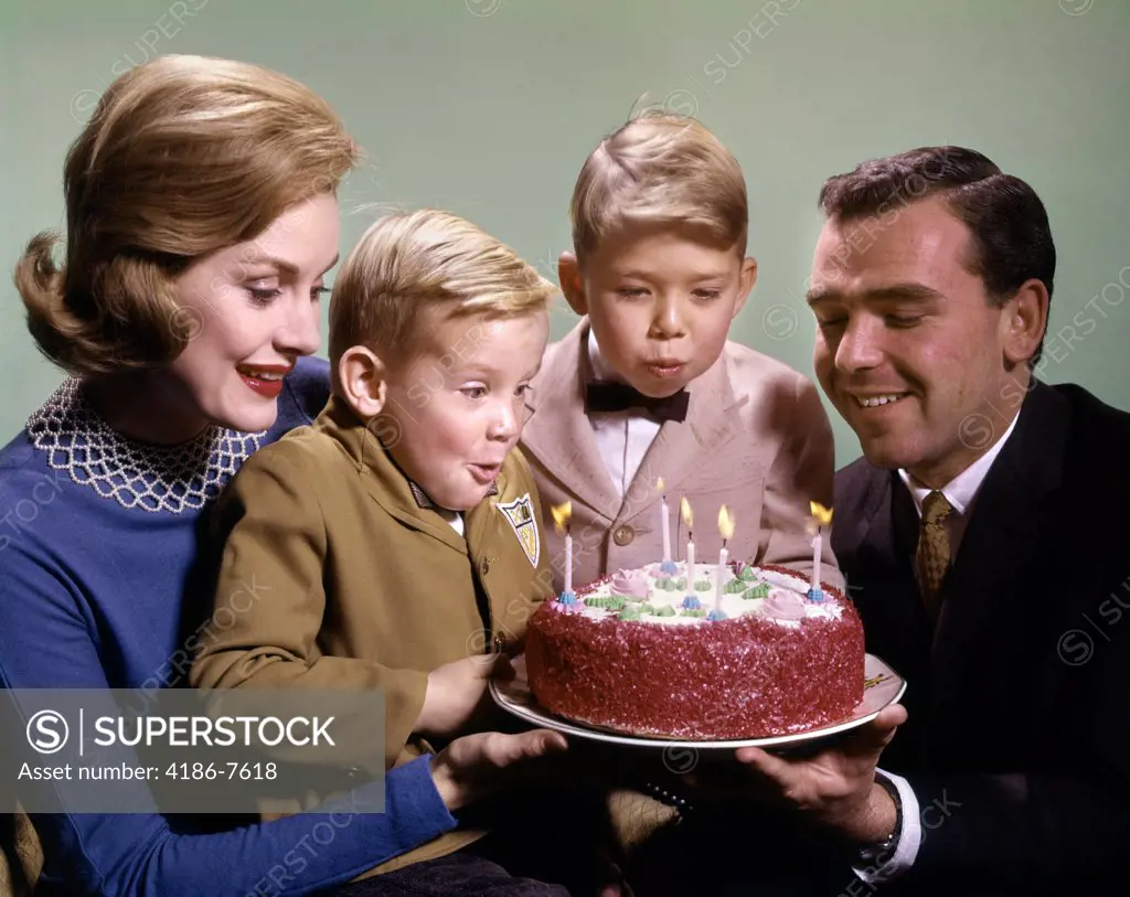 1960S Mother And Father Holding Birthday Cake And Sons Blowing Out Candles 
