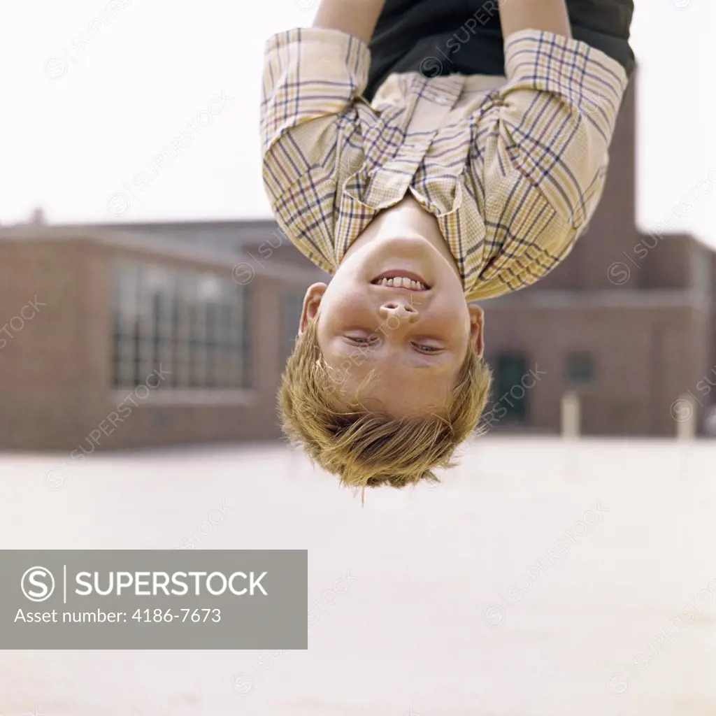 1960S Smiling Red Haired Boy Hanging Upside Down In Elementary School Yard