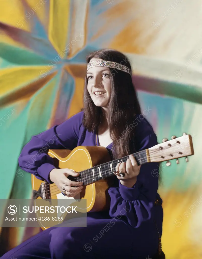 1970S Young Woman Wearing Purple Dress And Beaded Headband Playing Acoustic Guitar Patterned Background Folk Song
