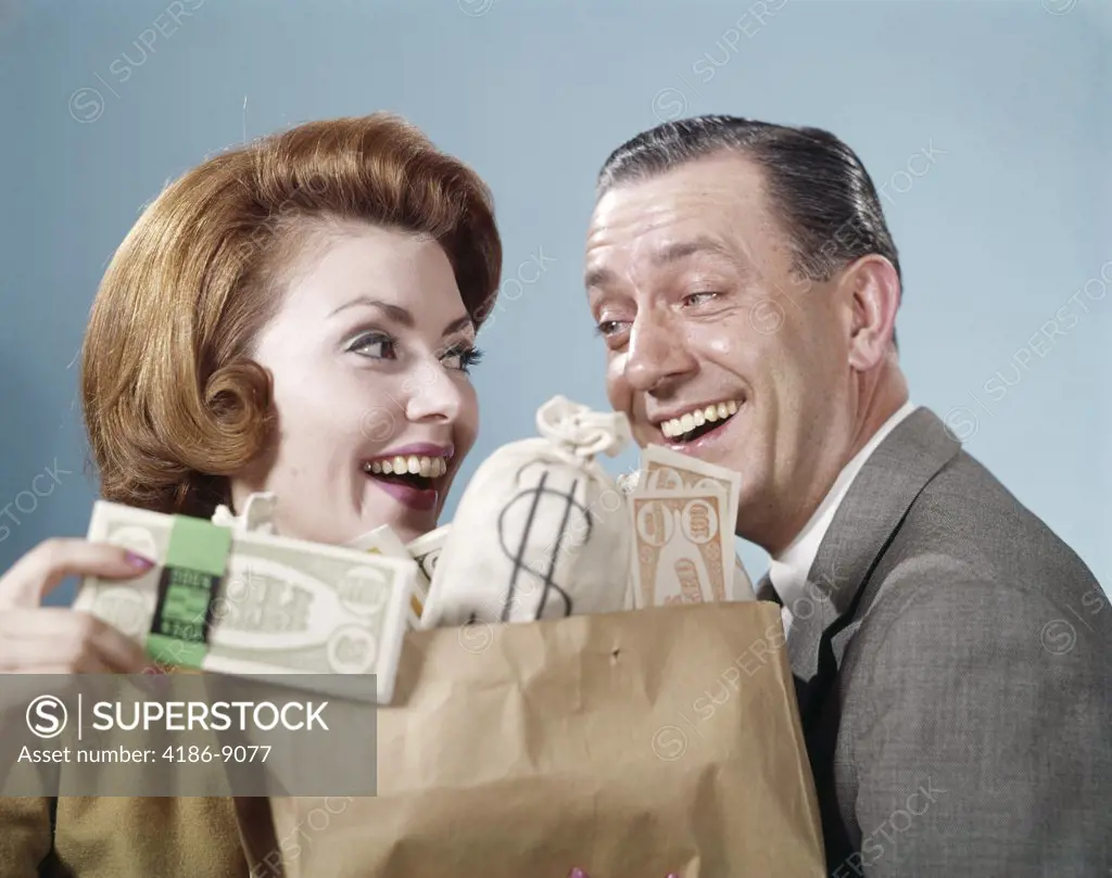 1960S Couple Man Woman Holding Shopping Bag Full Of Money Currency Smiling Happy Wealth Dollars Win Winnings Retro Humor