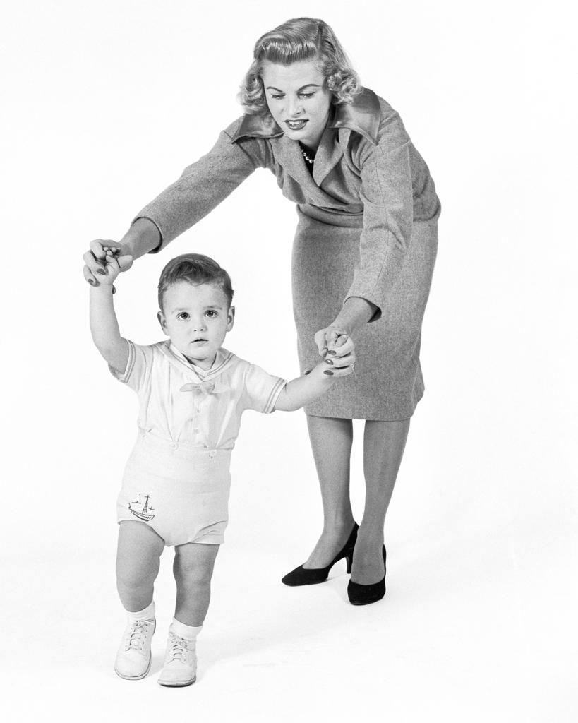 1950s 1960s CONCERNED PROUD MOTHER WATCHING HELPING BABY BOY TAKING FIRST STEPS WALKING LOOKING AT CAMERA
