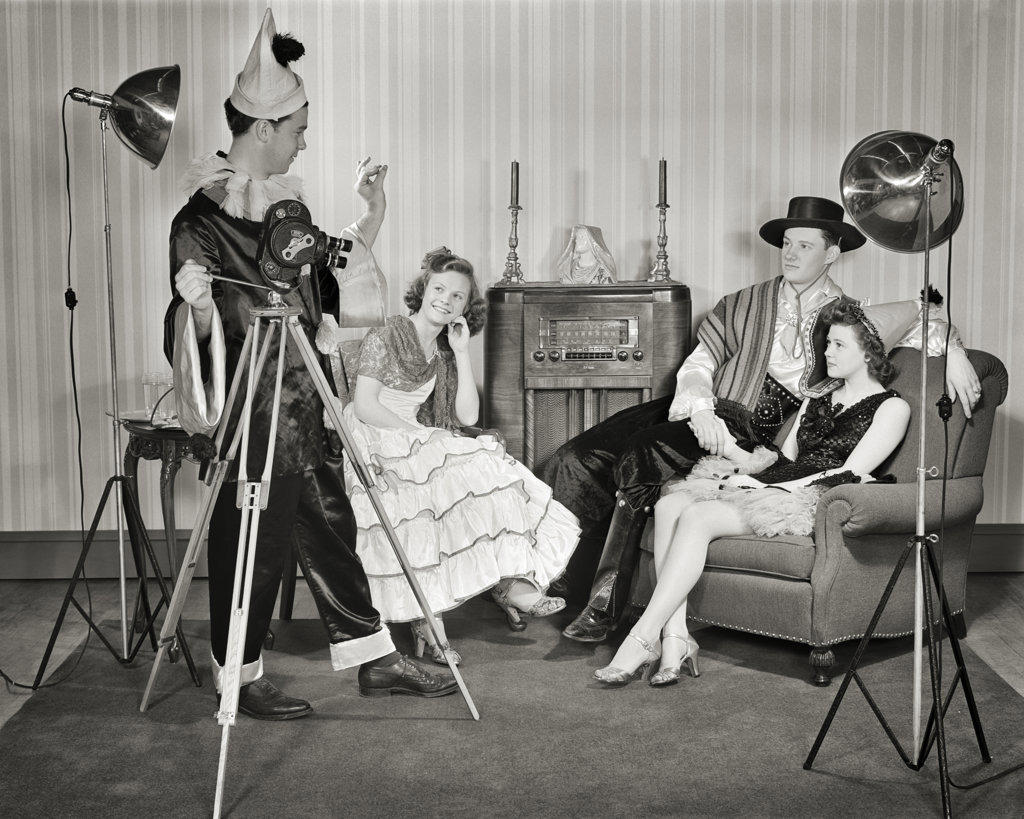 1940s GROUP OF YOUNG ADULTS COUPLES POSING WEARING PARTY COSTUMES MAN IN CLOWN COSTUME OPERATING HOME MOVIE CAMERA AND LIGHTS