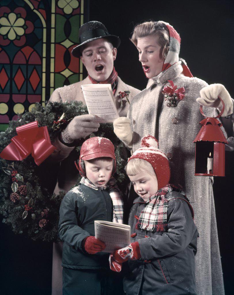 1950S Family Singing Carols Dad Man Has Wreath Over Arm Mom Woman Holds Red Lantern Boy Girl Music Song Snow Outdoor