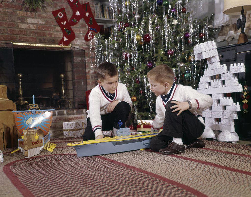1960S Two Brothers Playing With Toy Model Aircraft Carrier And Lego Blocks By Decorated Christmas Tree