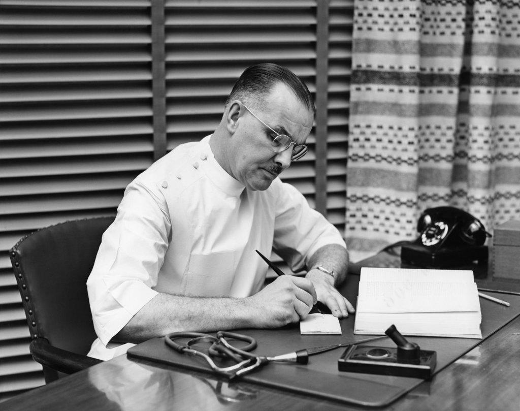 1940S Doctor Sitting At Desk Writing Prescription