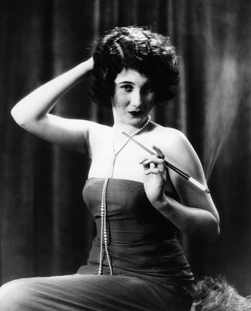 1920S Woman Wearing Strapless Gown And String Of Pearls Holding Long Cigarette Holder With Other Hand On Back Of Head
