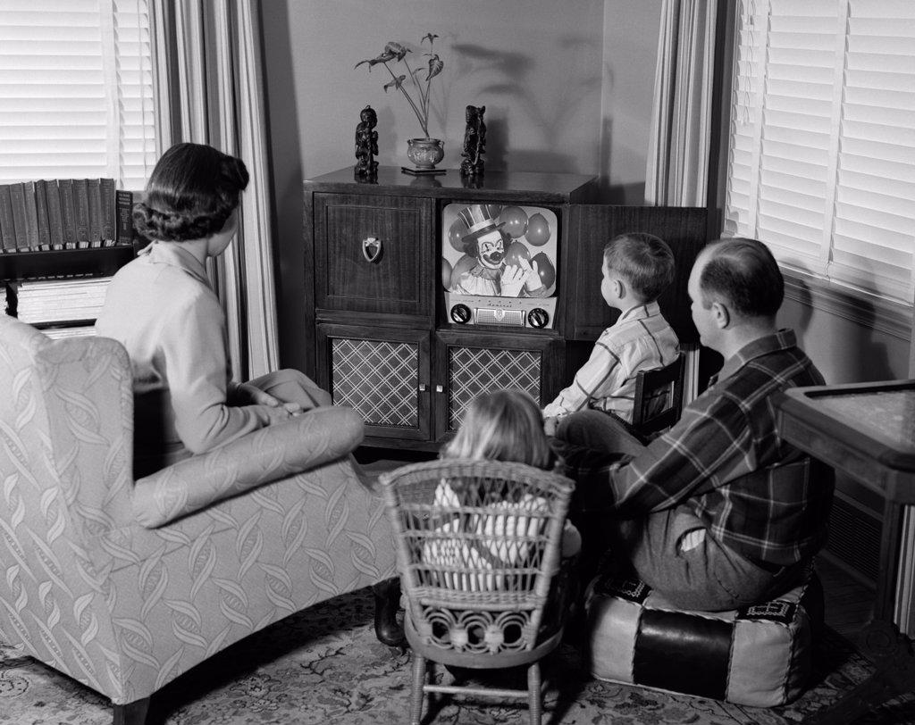 1950S Back View Of Family Of 4 Gathered Around Tv Set Watching Clown With Balloons