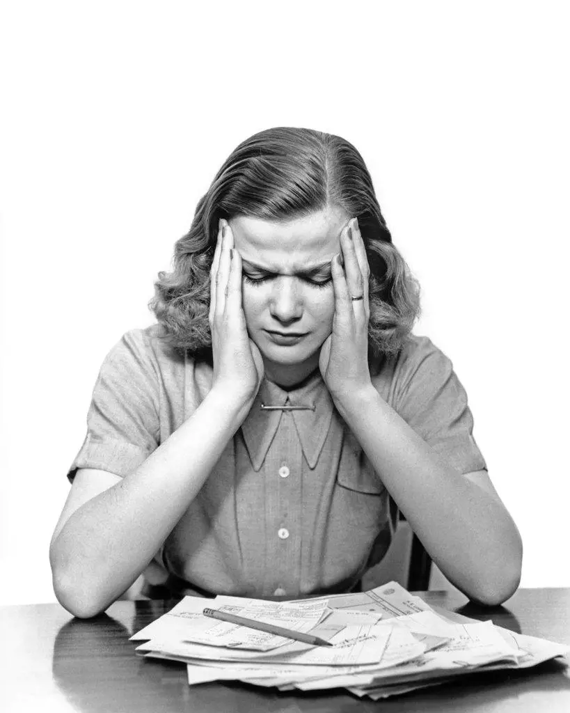 1940s PANIC STRICKEN OVERWHELMED WOMAN HOLDING HER HEAD LOOKING DOWN AT PILE OF UNPAID BILLS ON THE TABLE 