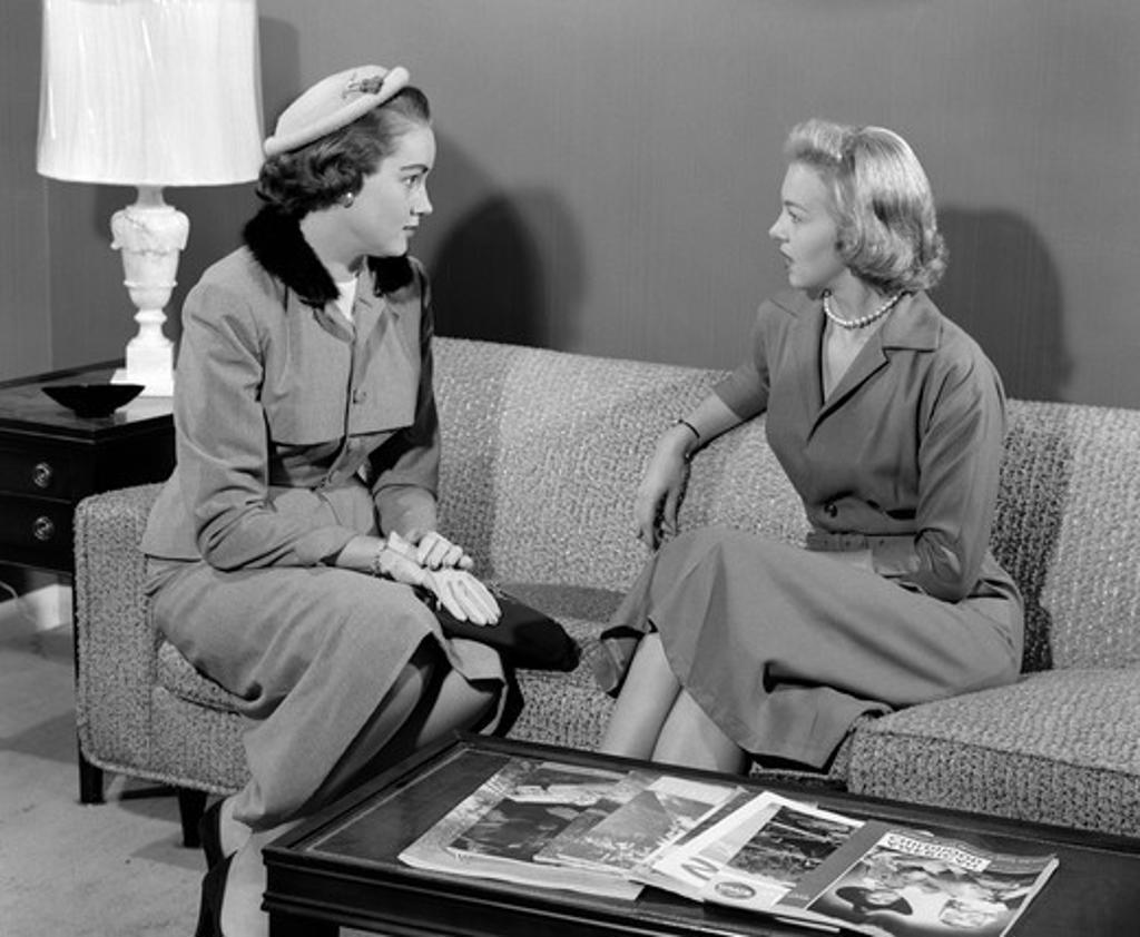 1950S Pair Of Women Sitting On Living Room Sofa Talking One Wearing Suit With Hat & Gloves