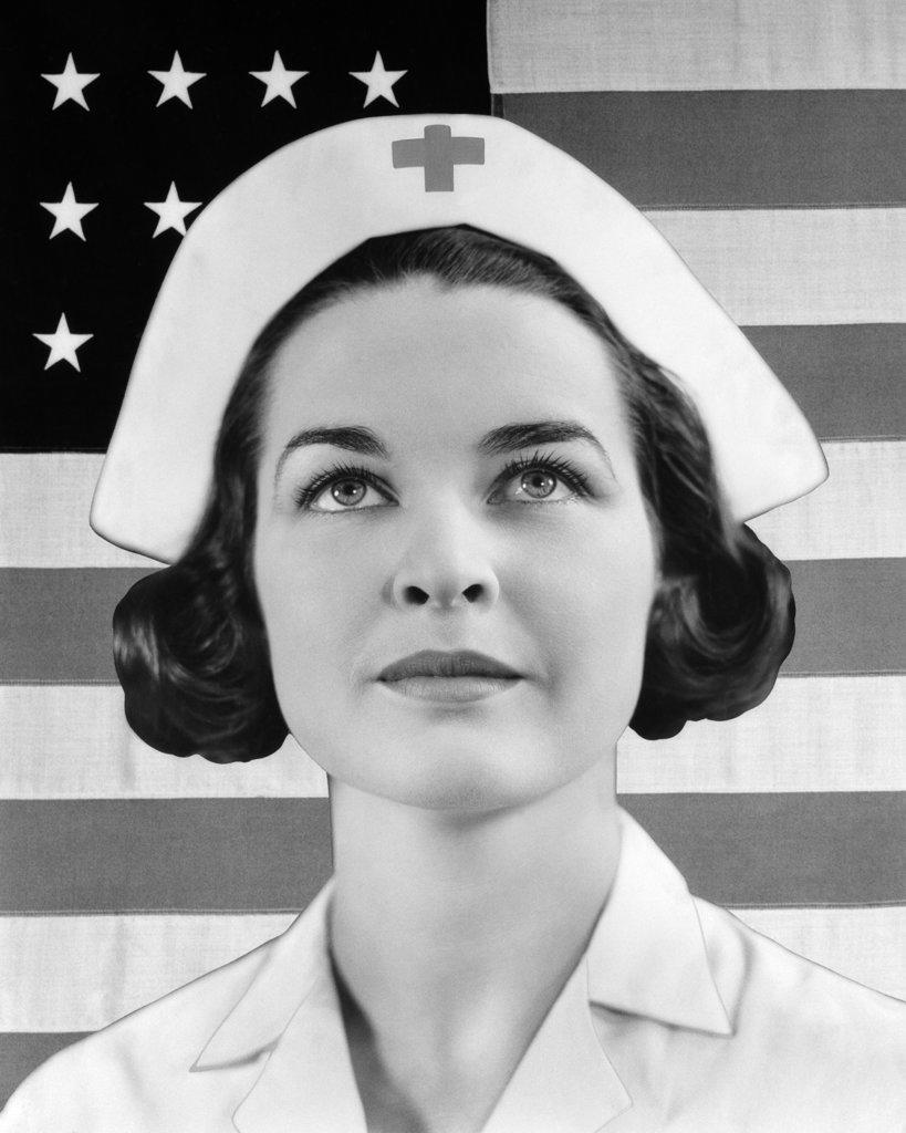 1930s 1940s PORTRAIT OF RED CROSS NURSE LOOKING UP WITH UNITED STATES FLAG BEHIND HER