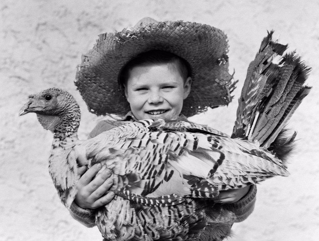 1940S Smiling Boy In Straw Farmer Hat Holding Turkey In Arms Looking At Camera