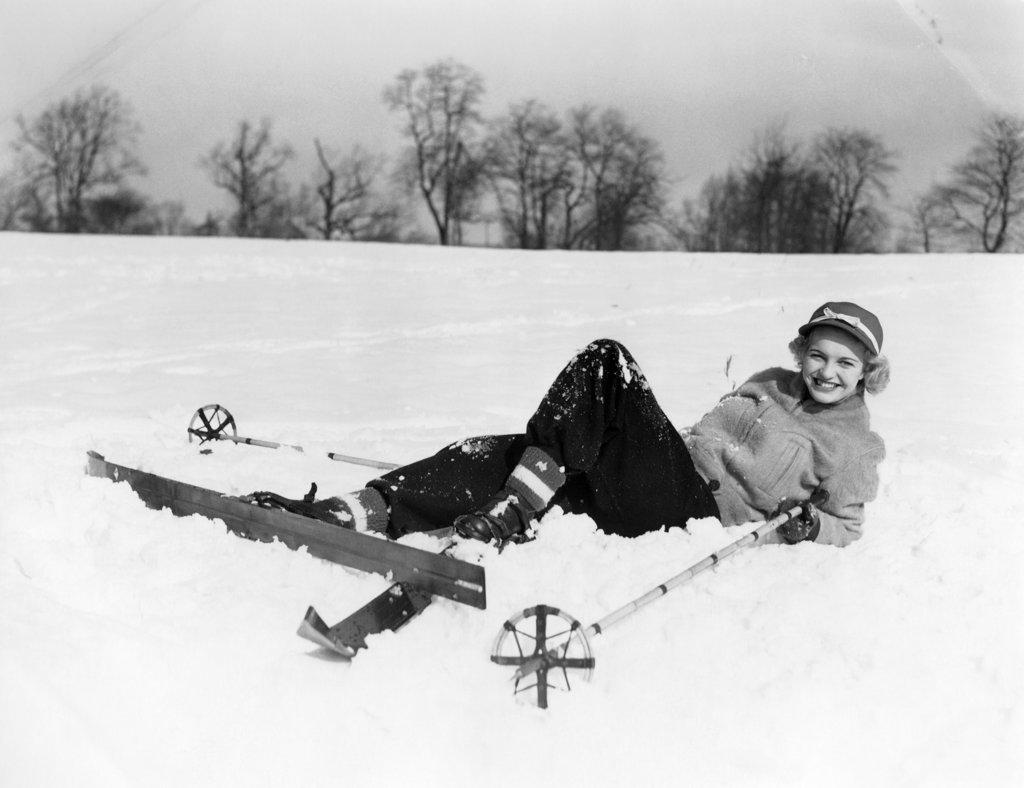 1940S 1950S Smiling Woman Beginner Skier In Ski Clothes And Cap Fallen Lying In Snow With Wood Skis And Bamboo Poles