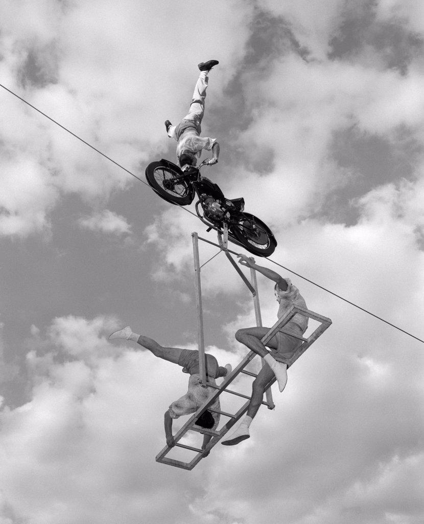 1960S High-Wire Act With Man Standing On His Head On Motorcycle & 2 Men On Ladder Below Him