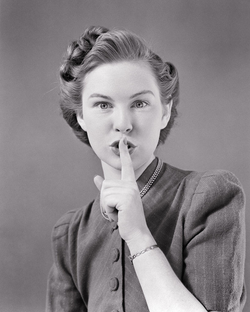 1940s PORTRAIT OF YOUNG WOMAN MAKING A SILENCE QUIET SHUSH GESTURE WITH INDEX FINGER TO HER LIPS LOOKING AT CAMERA 