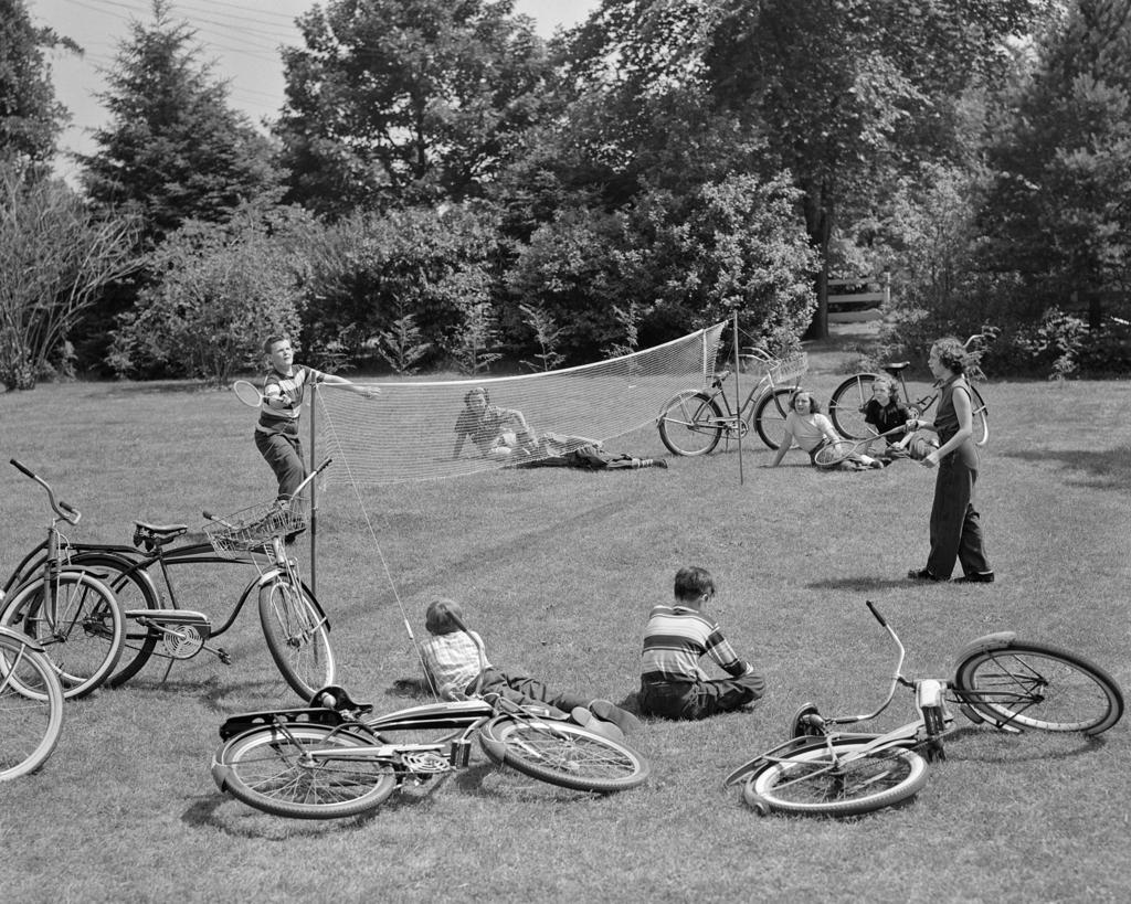 1950s GROUP OF TEENS LYING IN GRASS WITH BICYCLES BOY GIRL PLAYING BADMINTON 
