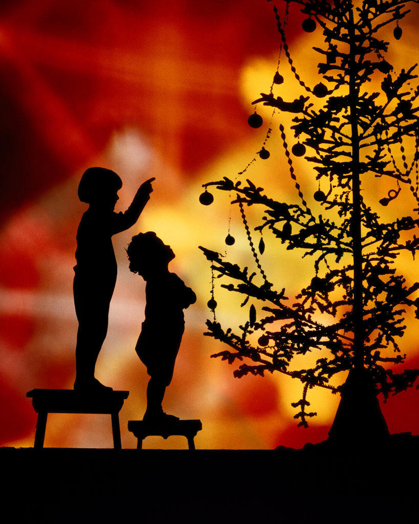 1920s TWO ANONYMOUS SILHOUETTED CHILDREN STANDING ON STOOLS LOOKING POINTING AT CHRISTMAS TREE COLORFUL SYMBOLIC BACKGROUND