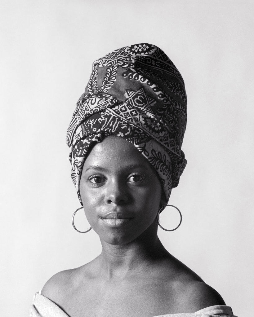 1970s PORTRAIT AFRICAN AMERICAN YOUNG WOMAN LOOKING AT CAMERA WEARING A TIGON A PRINT FABRIC HEAD-WRAP AND HOOP EARRINGS